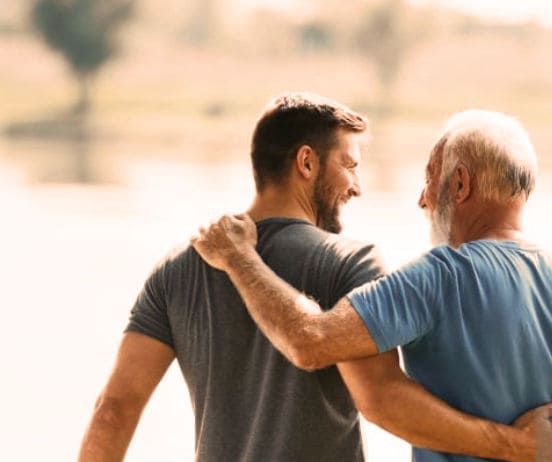 Nuori ja vanha mies kävelevät yhdessä ulkona, vanhempi laittaa käden nuoremman olkapäälle.