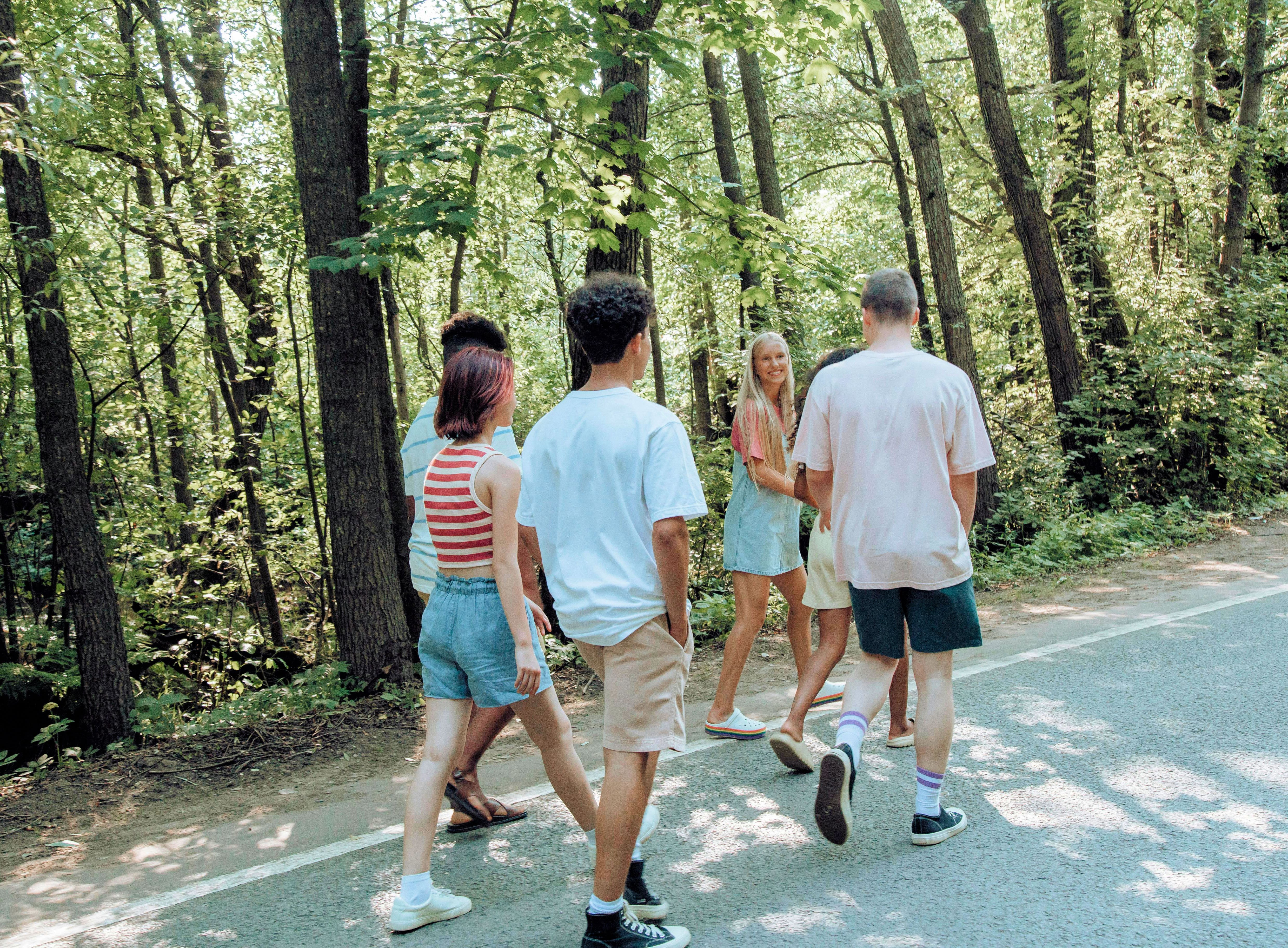 Ryhmä nuoria kävelee metsäpolulla kesäisessä ympäristössä.