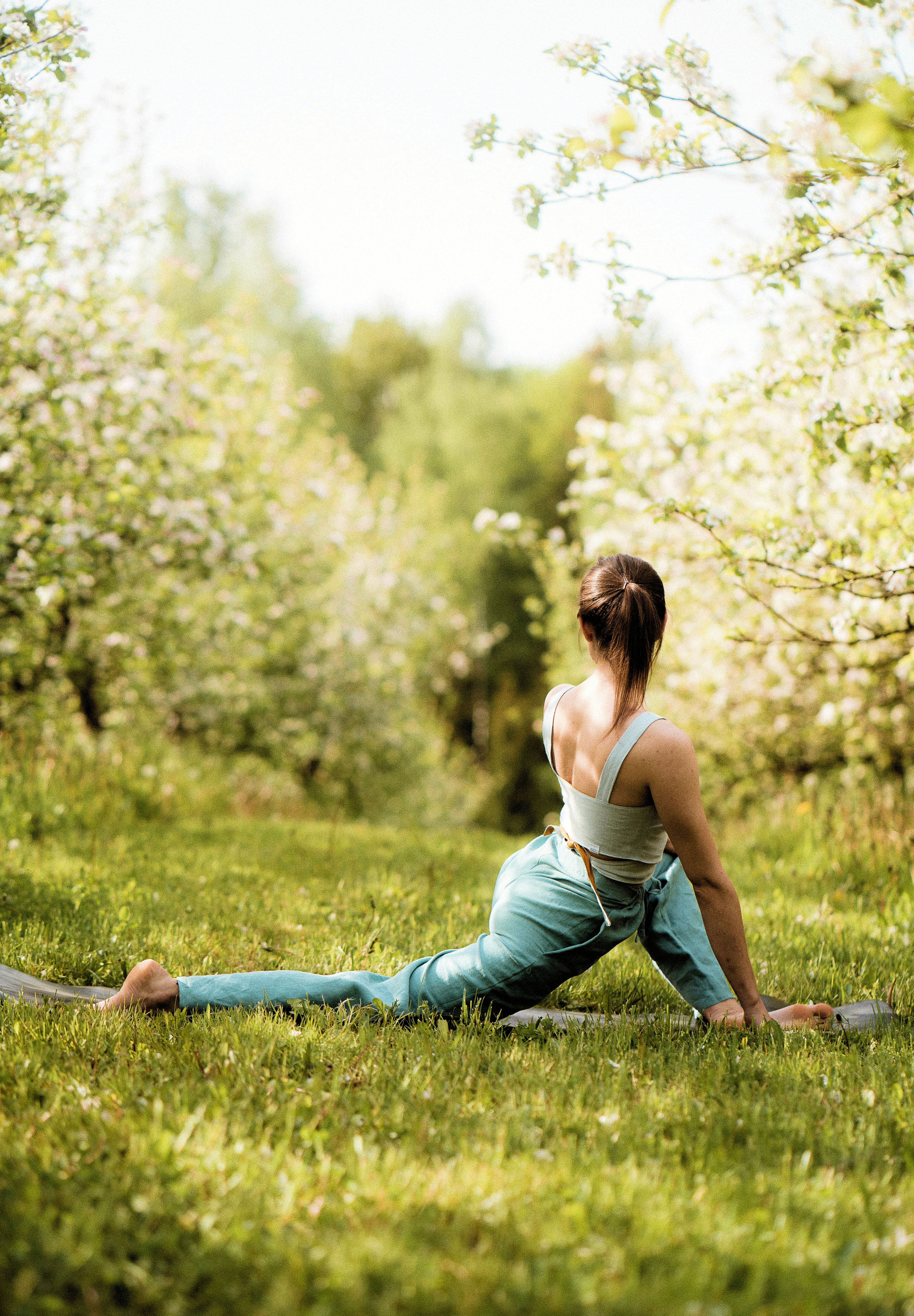Nainen venyttelee leveässä splitissä nurmikolla kukkivien puiden ympäröimänä.